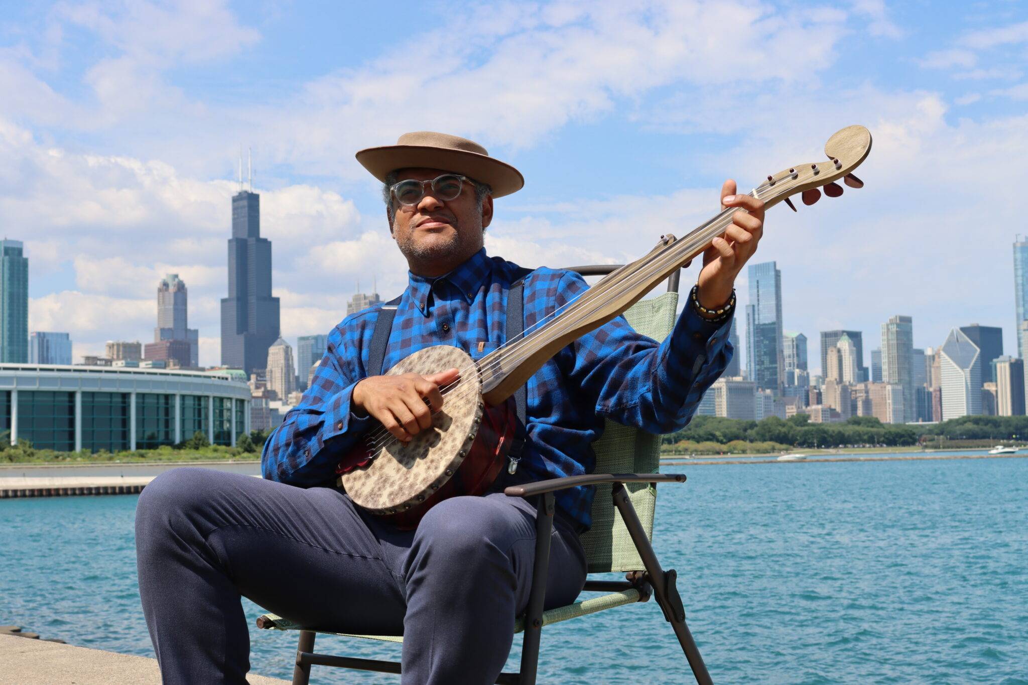 Dom Flemons plays banjo while sitting in front of the Chicago skyline