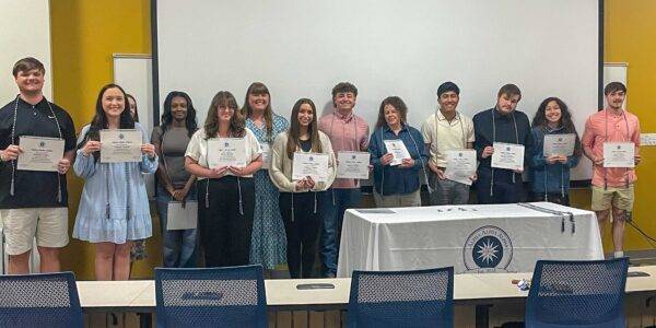 New inductees are lined up in two rows, holding their Alpa Alpha Alpha certificates in front of them.