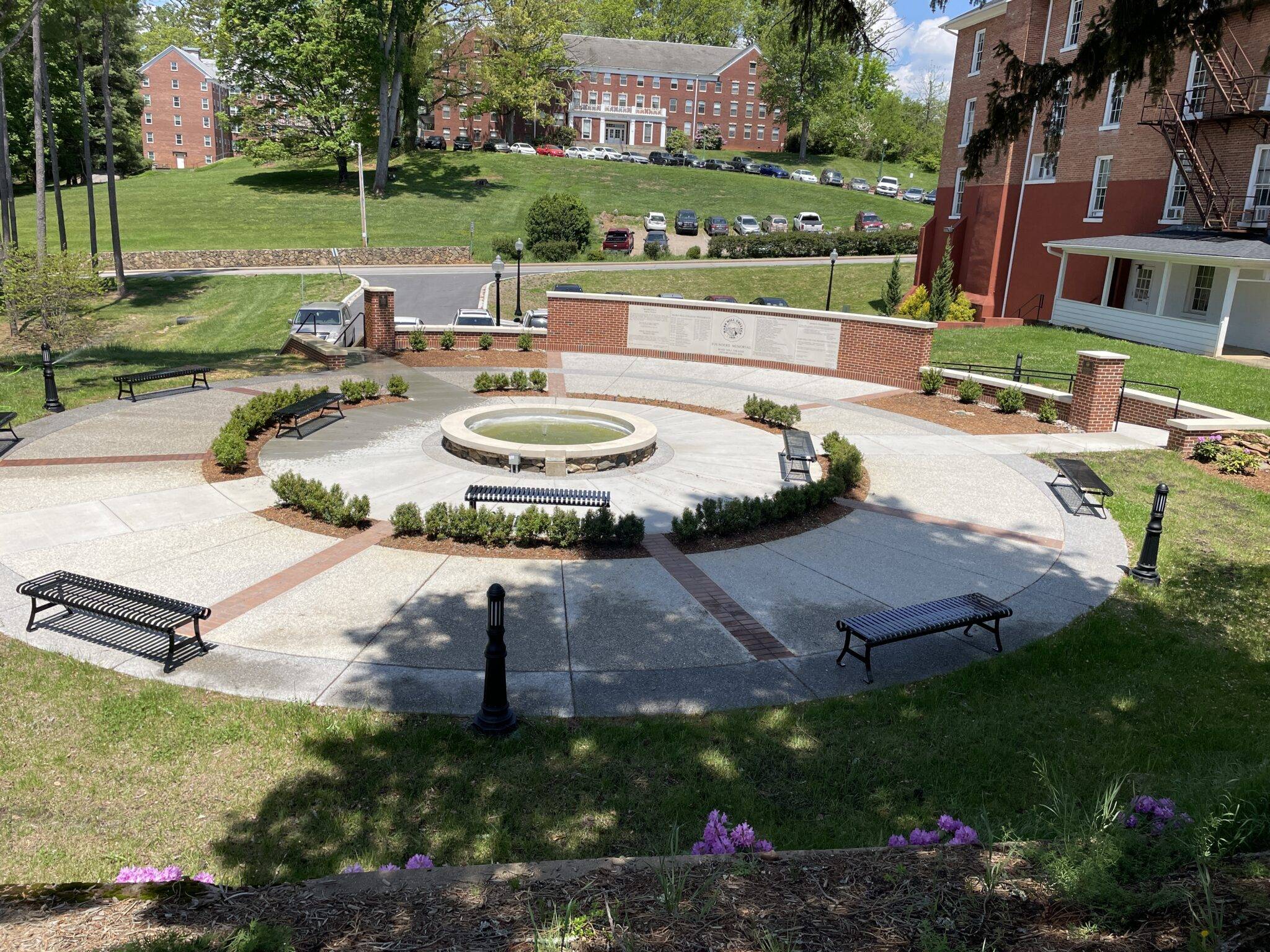 Sunken Garden with fountain in the center, surrounded by a ring of low bushes, with Founders Memorial wall behind.