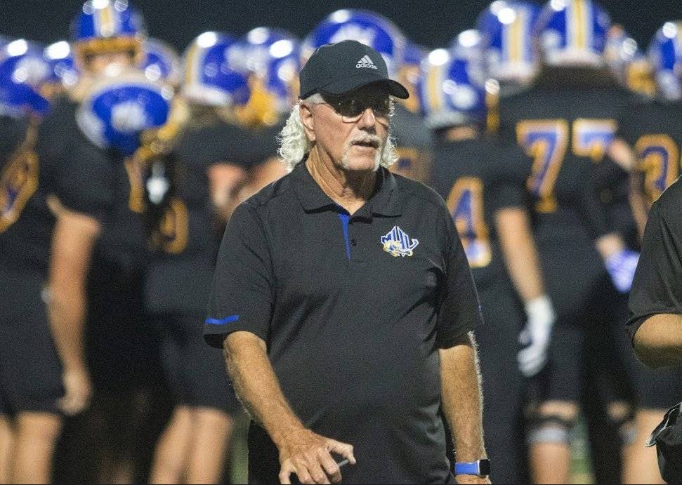 Coach Tim Clifton walks to the sidelines with the team huddled behind him