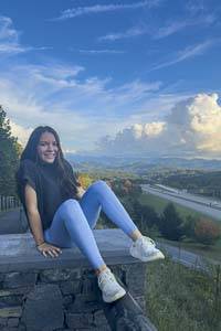 Abby Huff sits on a rock wall overlooking the interstate with an interesting sky of blue with white clouds behind her.