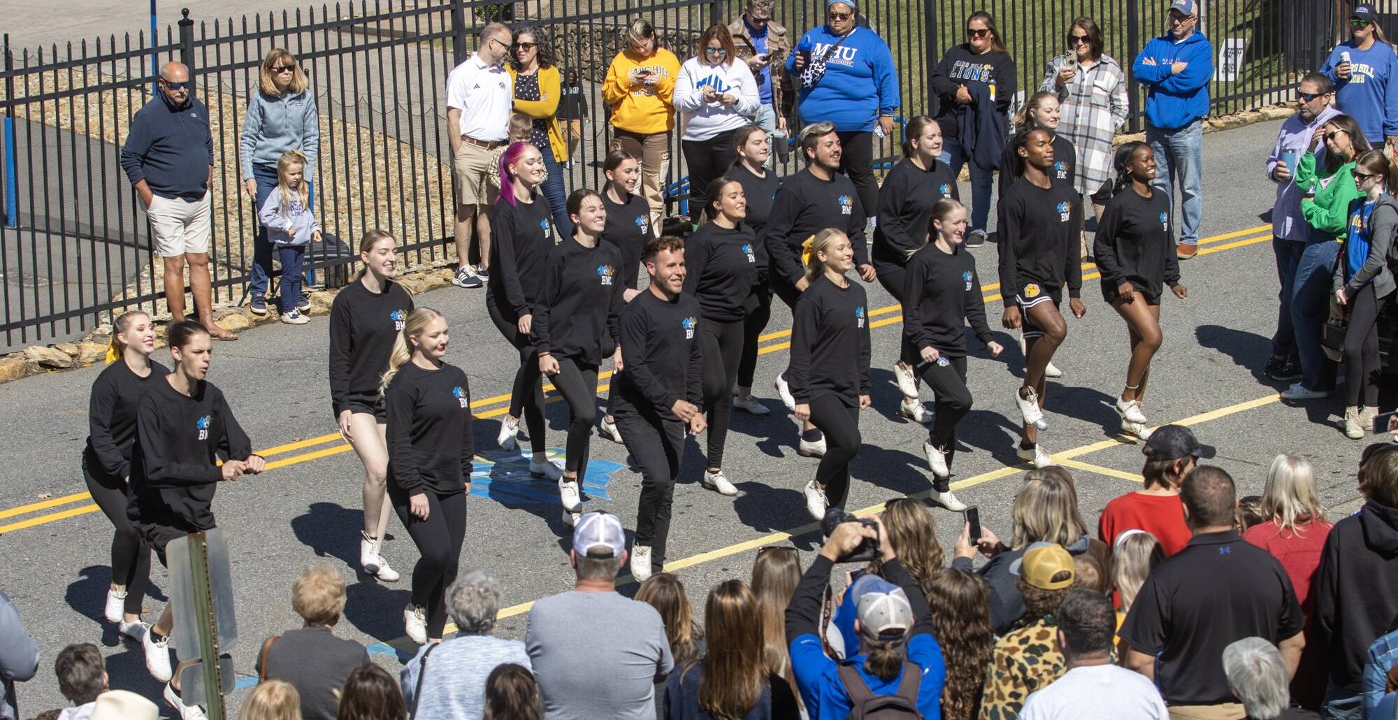 The Bailey Mtn. Cloggers, dressed in black t-shirts and black pants, dance on the street in front of Meare Stadium, as part of the homecoming festivities before the football game.