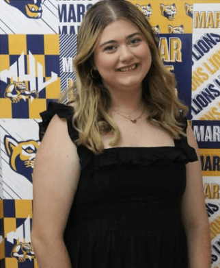 Sydney Grace stands in front of MHU backdrop with logos